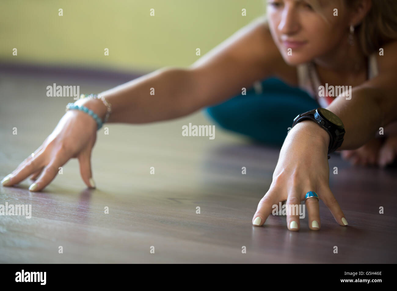 Sporty beautiful blond young woman working out indoors, doing Butterfly Pose, sitting in Bound Angle or Cobbler Posture Stock Photo