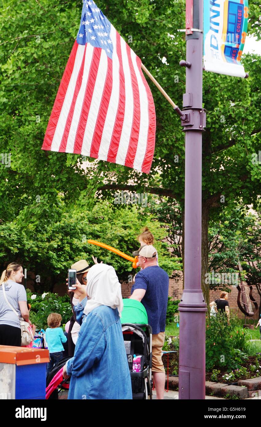 A Muslim woman in a headscarf walking under an American flag on the main street in the historic downtown of Ames, Iowa. Stock Photo