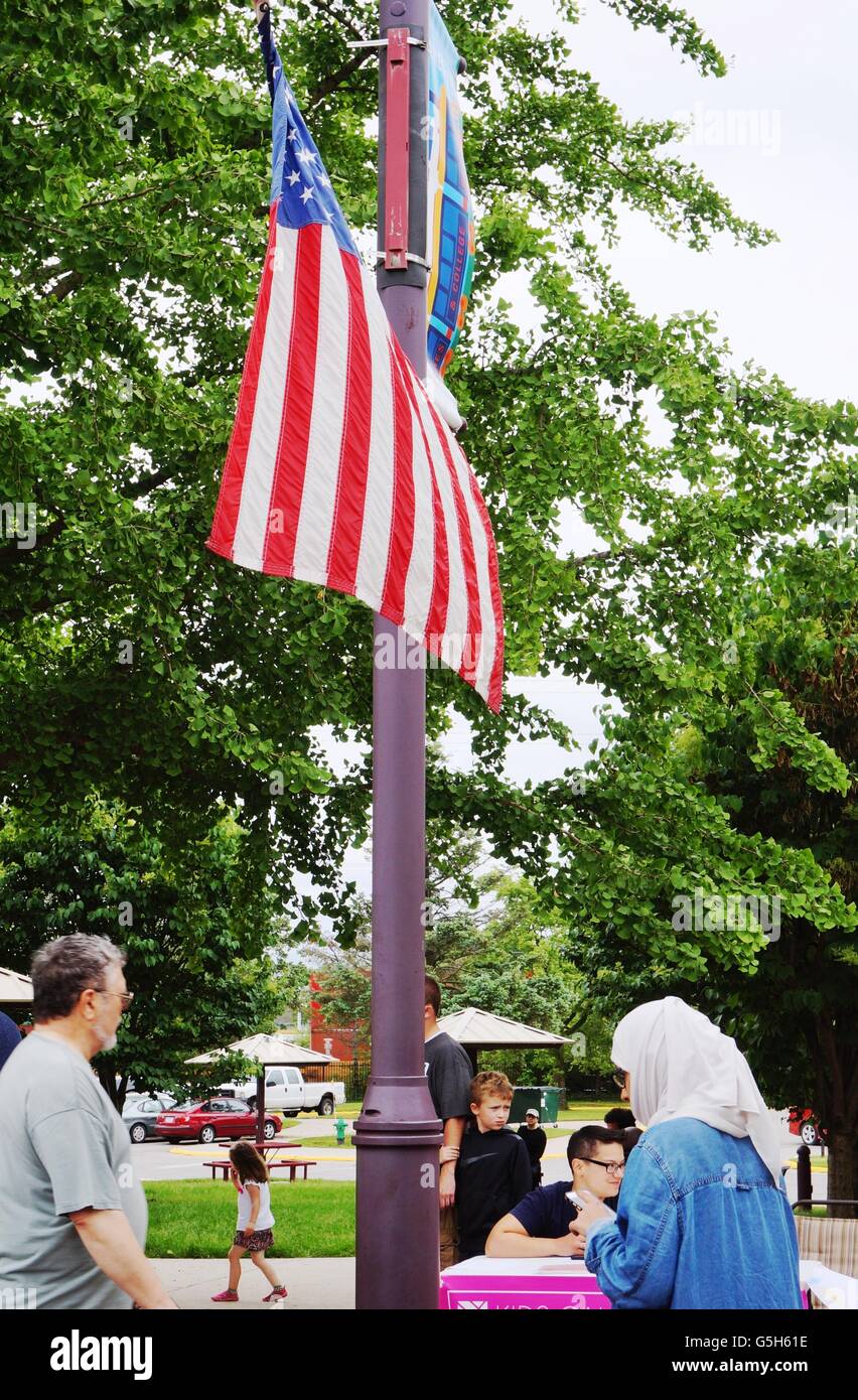 A Muslim woman in a headscarf walking under an American flag on the main street in the historic downtown of Ames, Iowa. Stock Photo