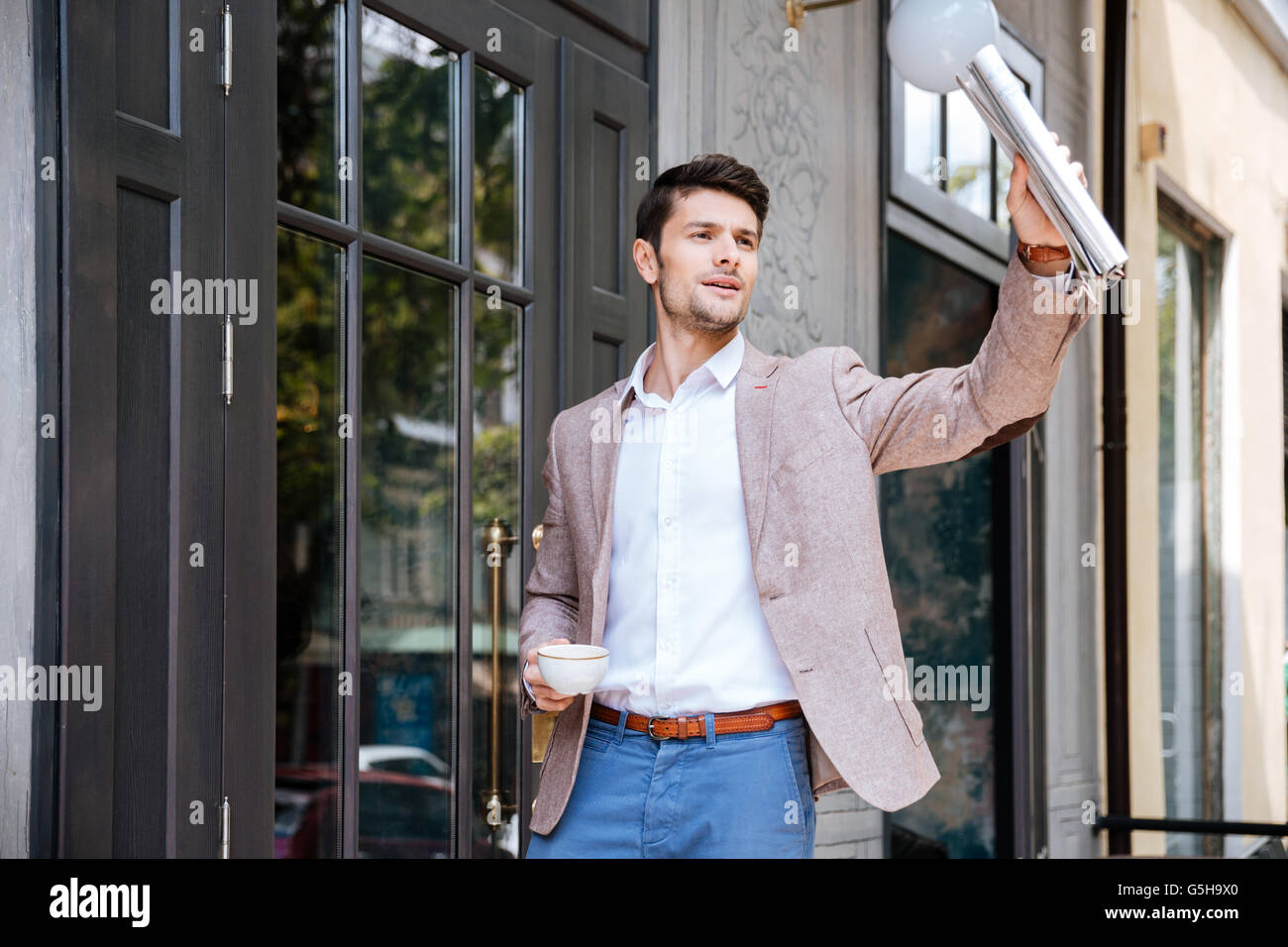 Young handsome businessman greeting someone at coffee shop outdoors Stock Photo