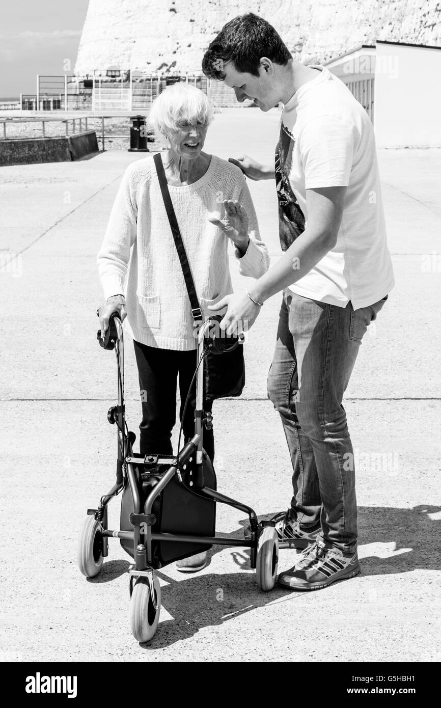 An Elderly Disabled Woman Using A Rollator Walking Aid Helped By Her Grandson, Brighton, Sussex, UK Stock Photo