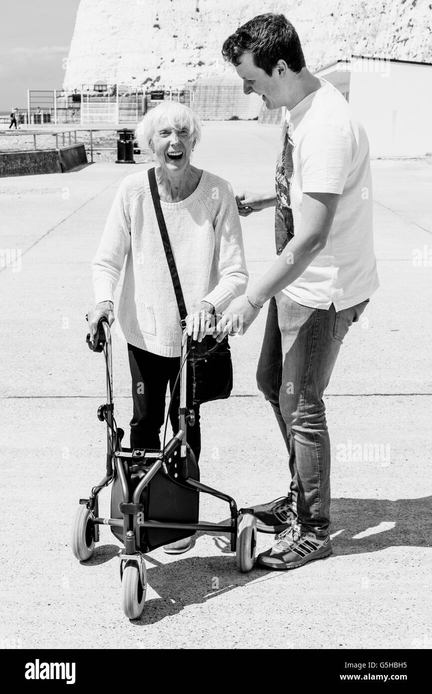 An Elderly Disabled Woman Using A Rollator Walking Aid Helped By Her Grandson, Brighton, Sussex, UK Stock Photo