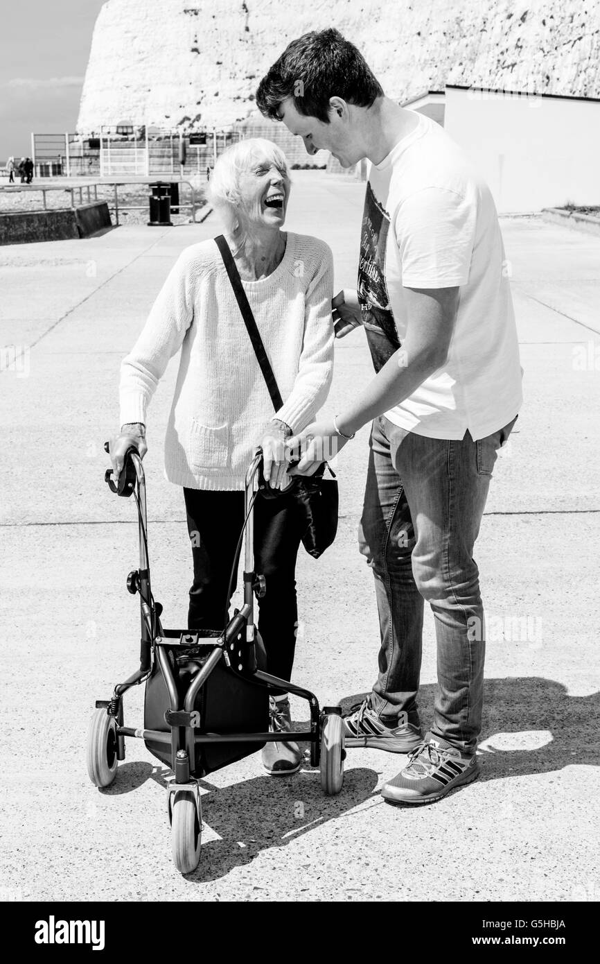 An Elderly Disabled Woman Using A Rollator Walking Aid Helped By Her Grandson, Brighton, Sussex, UK Stock Photo