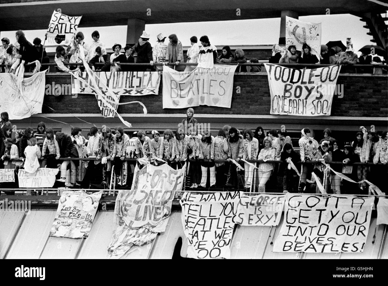 Huge Banners draped from the rails of the viewing galleries at the Queen's Building as hundreds of fans give a loyal send off to the Beatles at London Airport. One banner proclaims 'We love you Beatles'. The group are stting off for a tour in the United States. Stock Photo