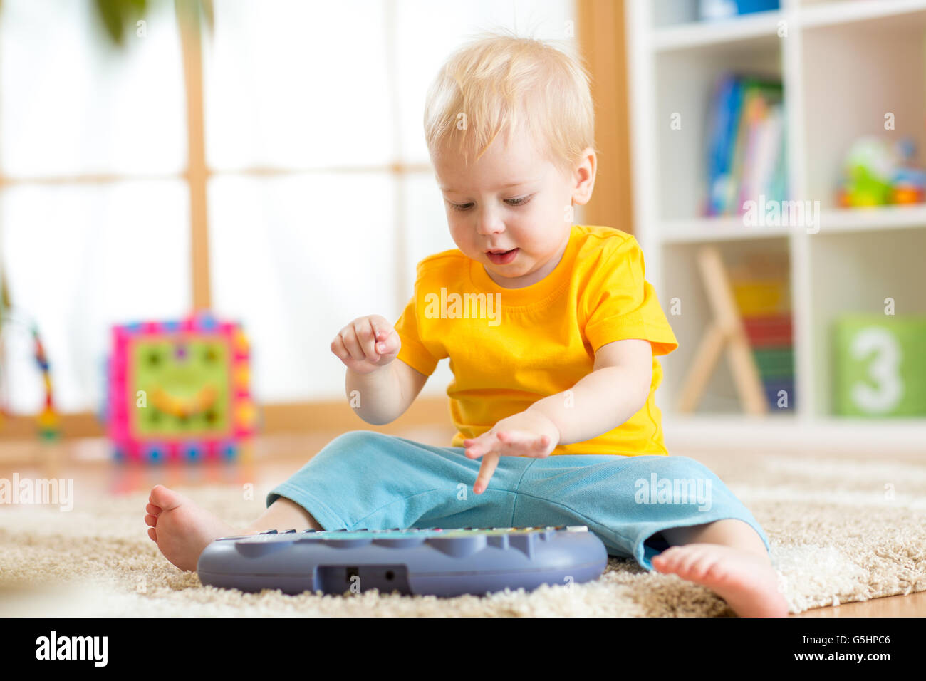 Happy kid boy playing piano toy in nursery Stock Photo