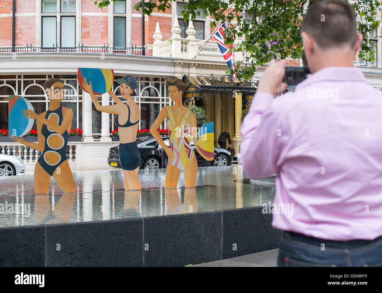 A member of the public takes a photograph of Chance, a cutout sculpture by artist Alex Katz featured inside the Tadao Ando-designed water feature outside The Connaught Hotel in London, where it will remain for the day and then be transferred to Timothy Taylor art gallery in London, where it can be seen until Saturday 3 September. Stock Photo