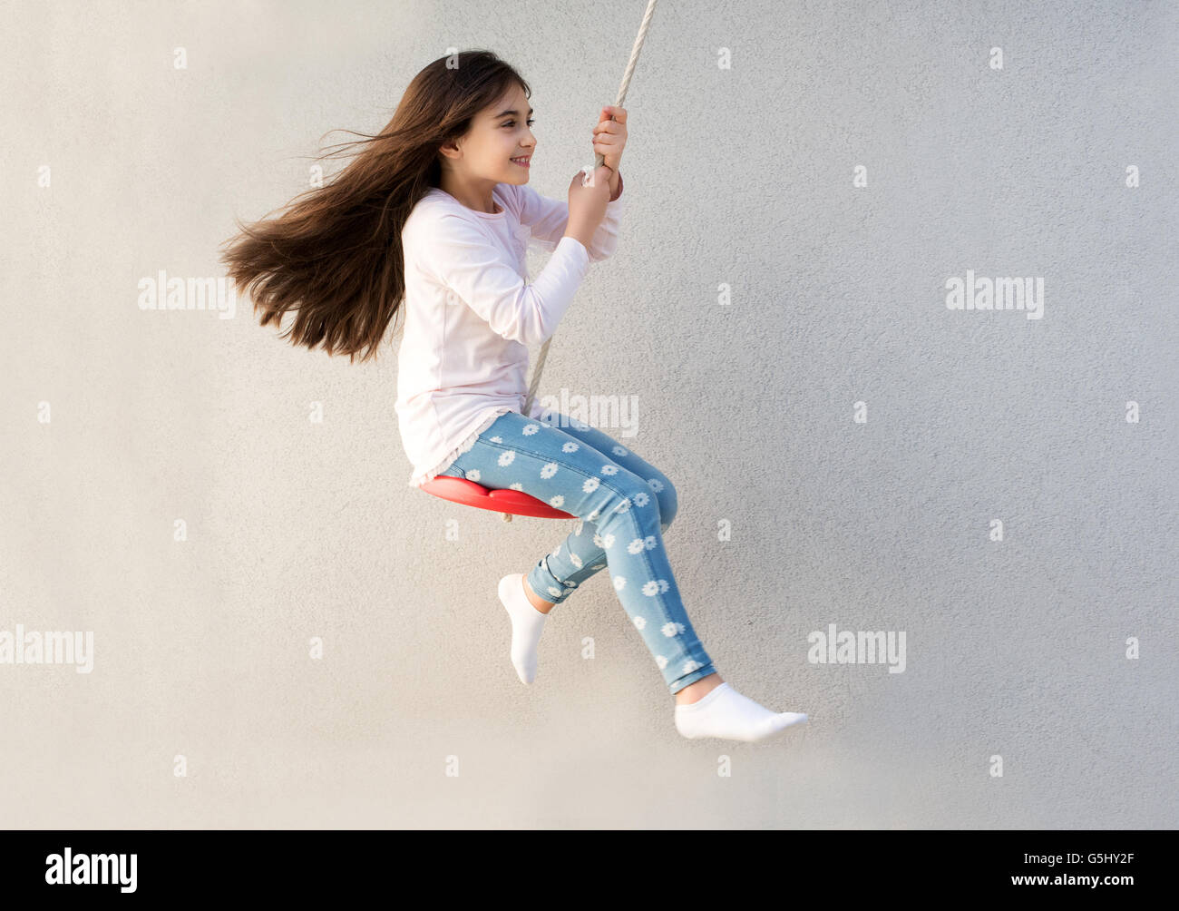Happy little girl playing on a swing with her long hair flowing out ...