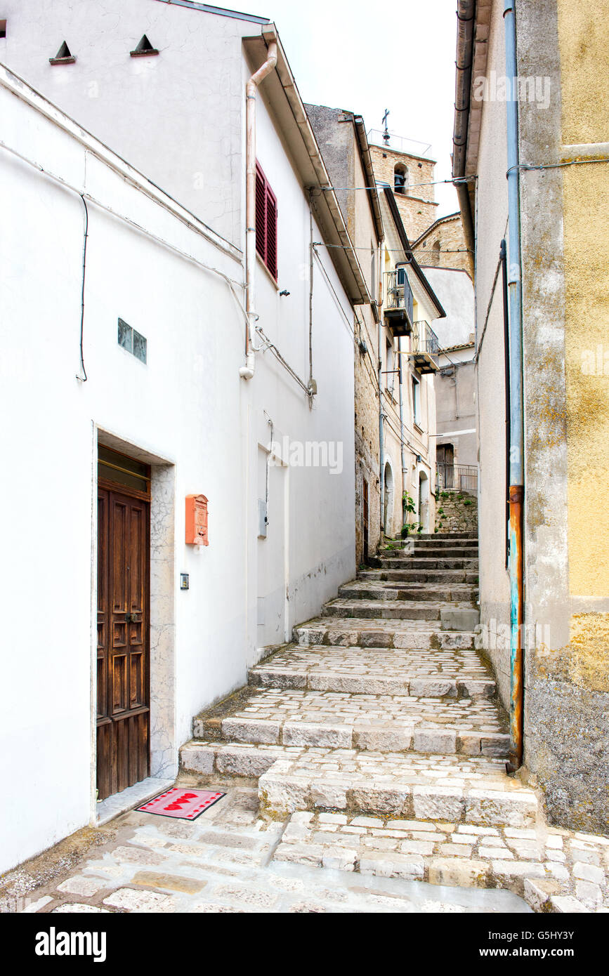 Narrow old cobbled street with steps leading up the hill between buildings in a village, view from the bottom looking up Stock Photo
