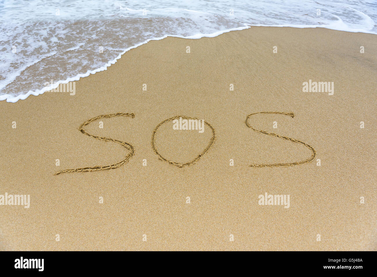 Word SOS on the beach against the backdrop of the sea waves. Stock Photo