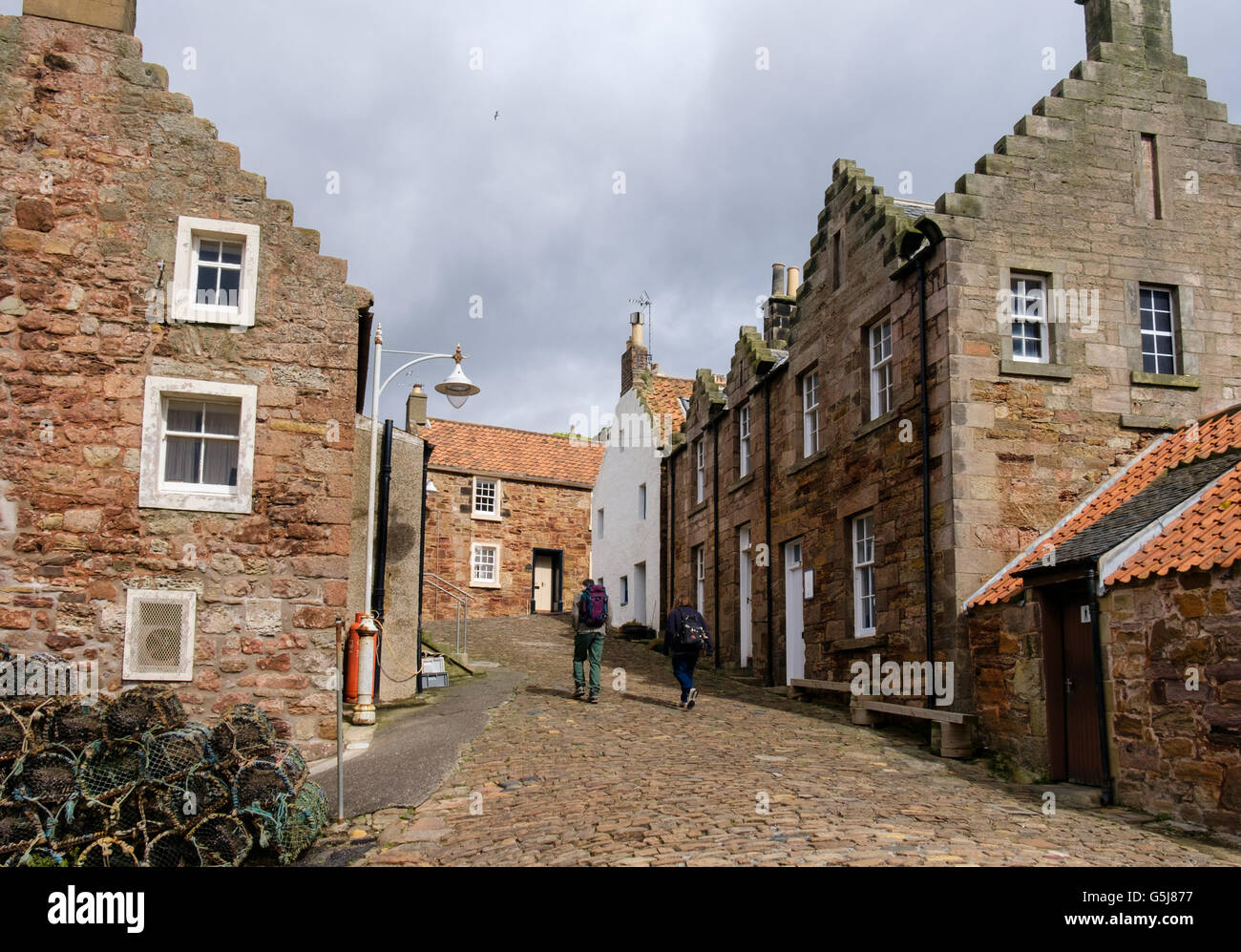 Old cottages with hikers walking up cobbled street in historic fishing village near harbour. Crail East Neuk Fife Scotland UK Stock Photo