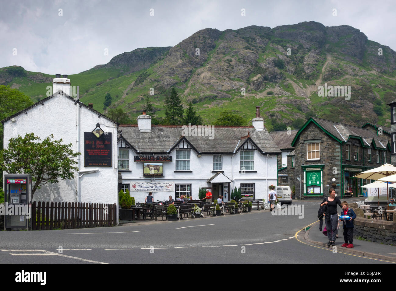 The Black Bull Hotel and Village Store with Fells Coniston  Cumbria England UK with dark rain clouds Stock Photo