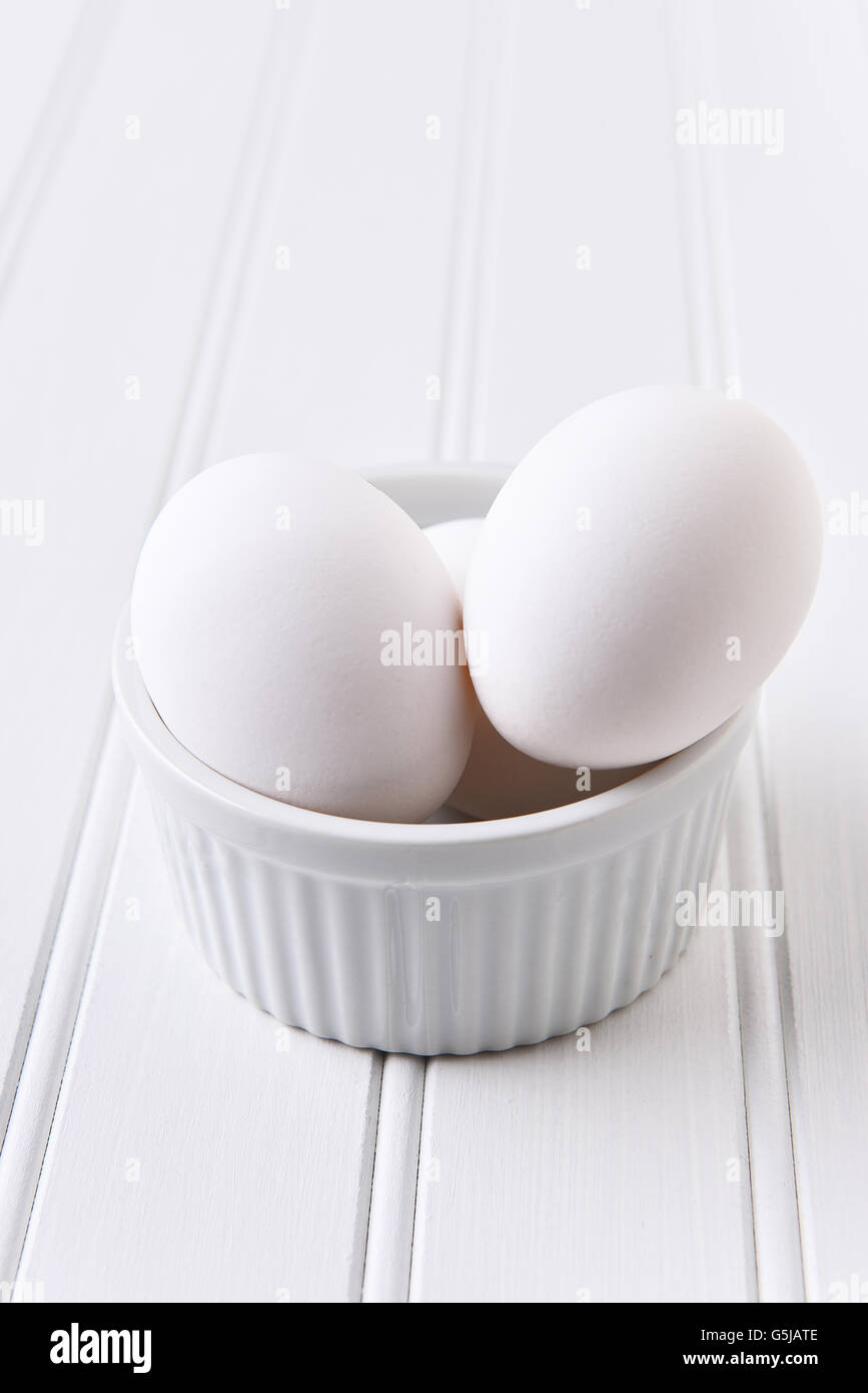 Egg White on White Still Life. Eggs in a ramekin on a white table. Vertical format with copy space. Stock Photo