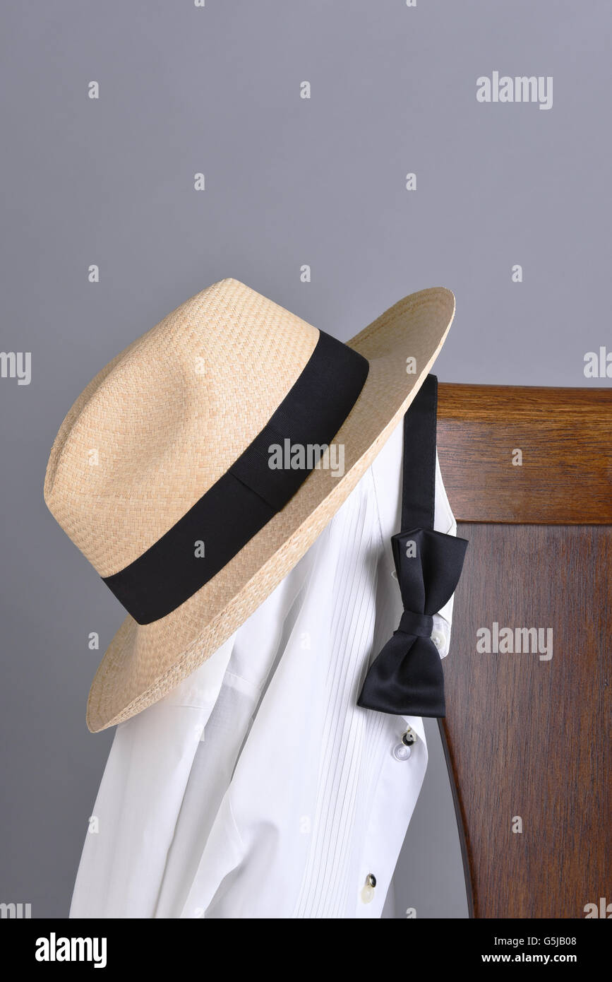Closeup of a hat and tuxedo shirt hung on a chair back with a black bow tie. Vertical format with copy space. Stock Photo