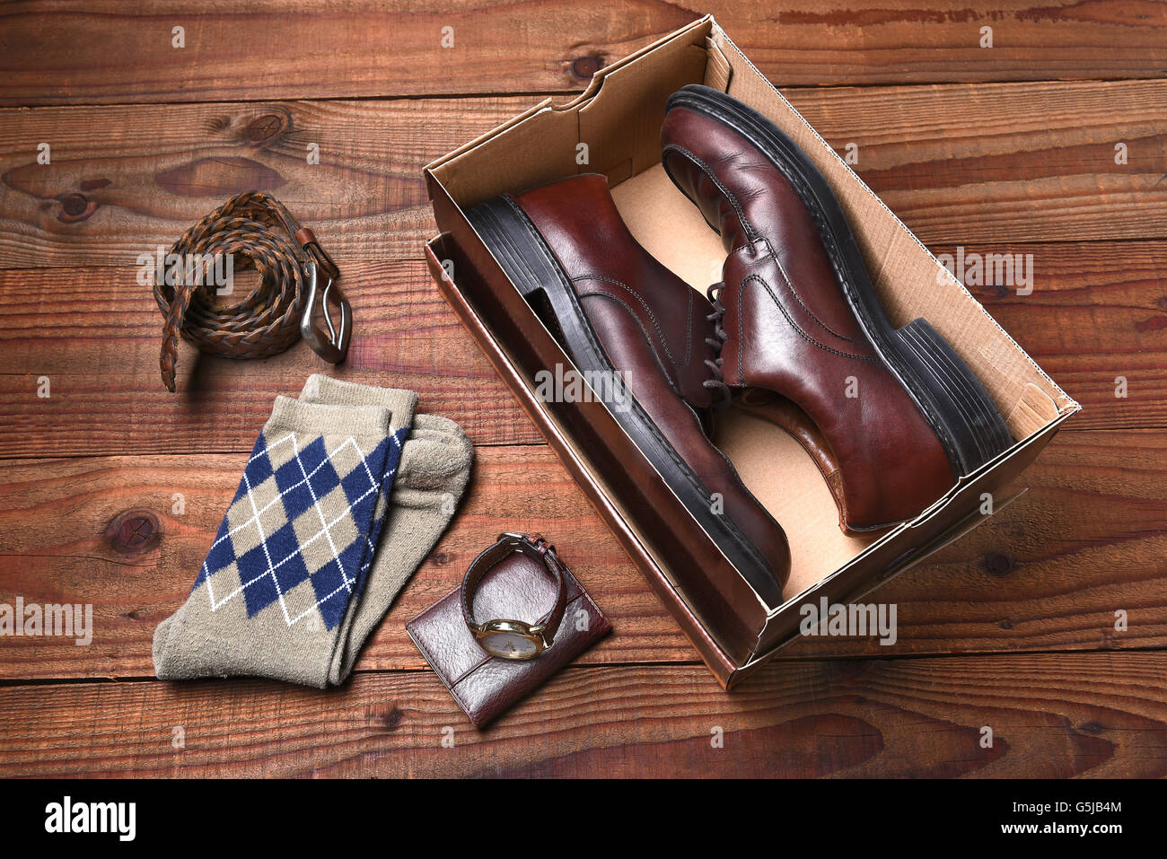 Overhead view of a pair of men's shoes in a shoebox. Socks, belt, watch and wallet lie on the floor next to the box. Stock Photo
