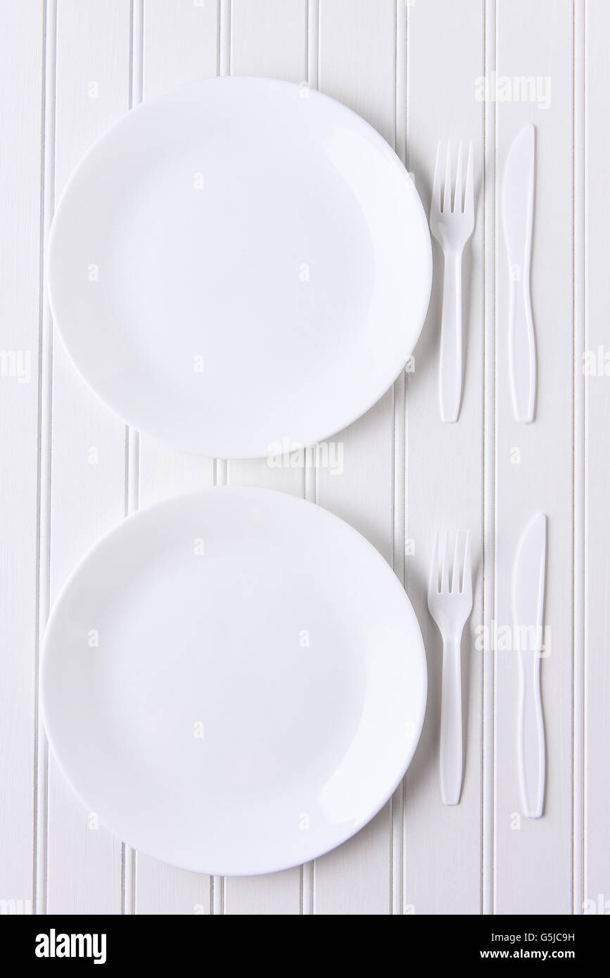 Top view of an all white place setting. White plates and plastic utensils on a white background. Stock Photo