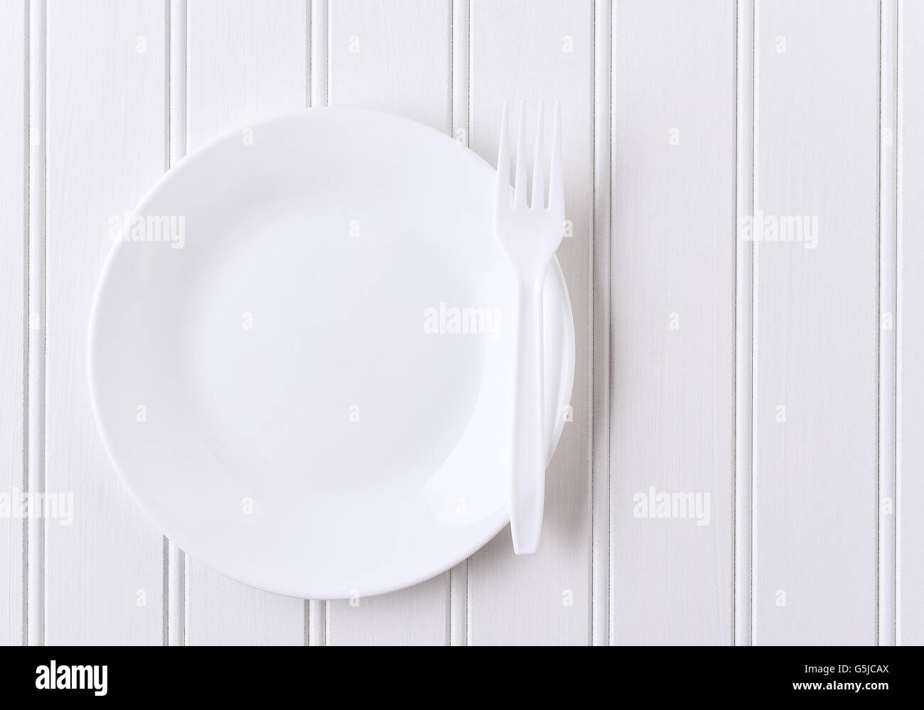 Top view of a white plate and white plastic fork on a white beadboard surface. Horizontal format with copy space. Stock Photo