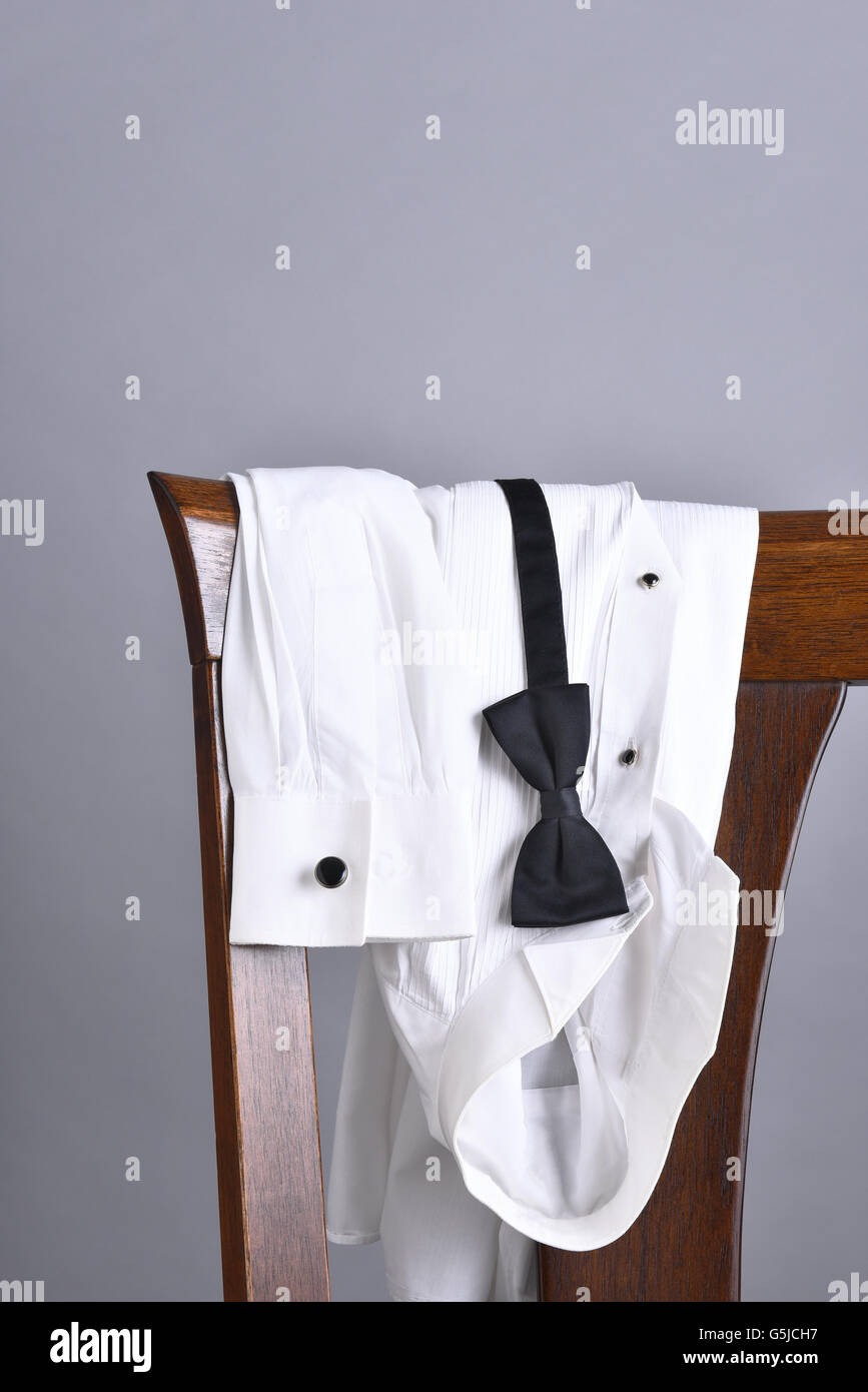 Closeup of a tuxedo shirt draped over a chair back with a black bow tie. Vertical format with copy space. Stock Photo