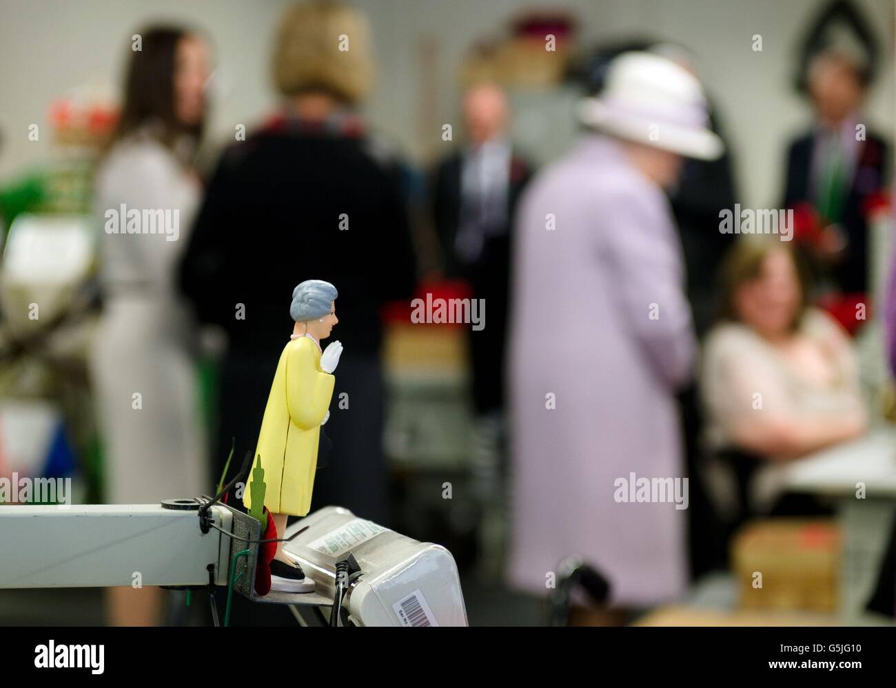 A solar-powered model of Britain's Queen Elizabeth II is seen as the Queen herself watches an employee of The Poppy Factory making the red emblem of the British Legion's annual poppy appeal, during a visit to the company headquarters in Richmond, London. Stock Photo