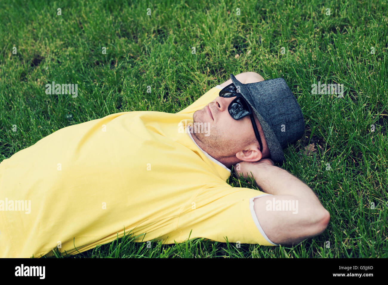 man in a yellow T-shirt and hat lying on the grass Stock Photo
