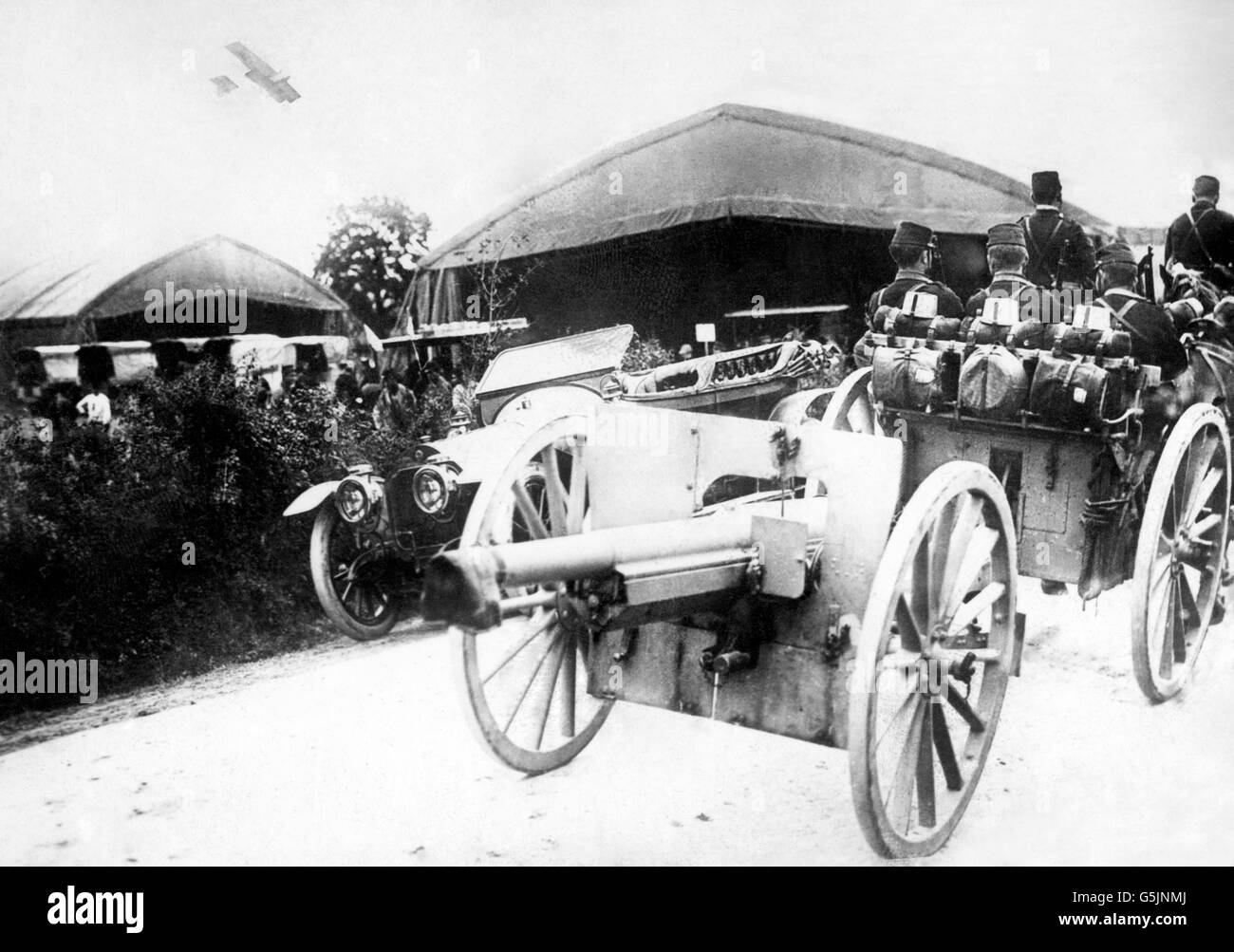 A French 75 gun passing through a village in France, with a Farman biplane overhead acting as scout. Stock Photo