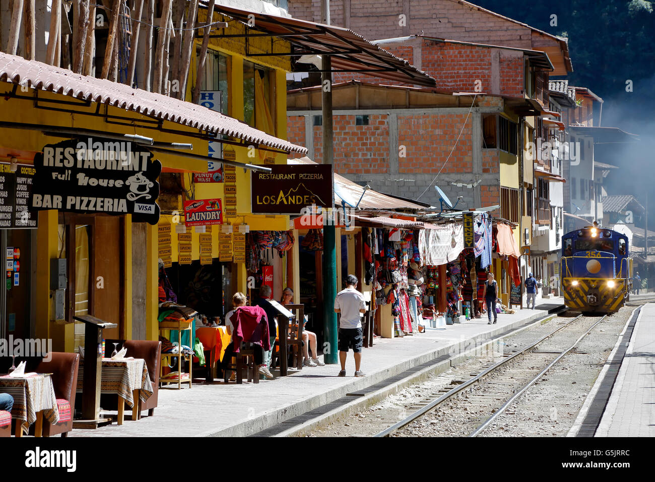 Train going by shops and restaurants, Machu Picchu Pueblo (fka Aguas Calientes), Cusco, Peru Stock Photo