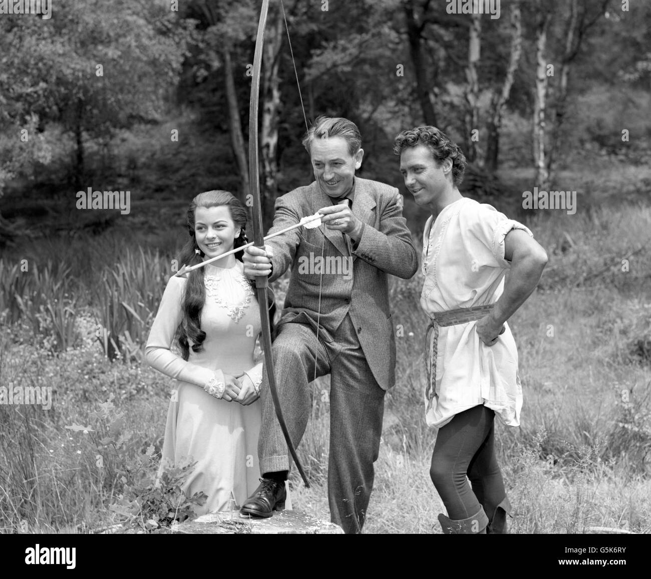 Filmland's Walt Disney, centre, shows a deft touch with a bow and arrow to Robin Hood actor Richard Todd and Maid Marian actress Joan Rice during a visit to the film unit of the new live-action production of Robin Hood on location at Burnham Beeches, Buckinghamshire. Stock Photo