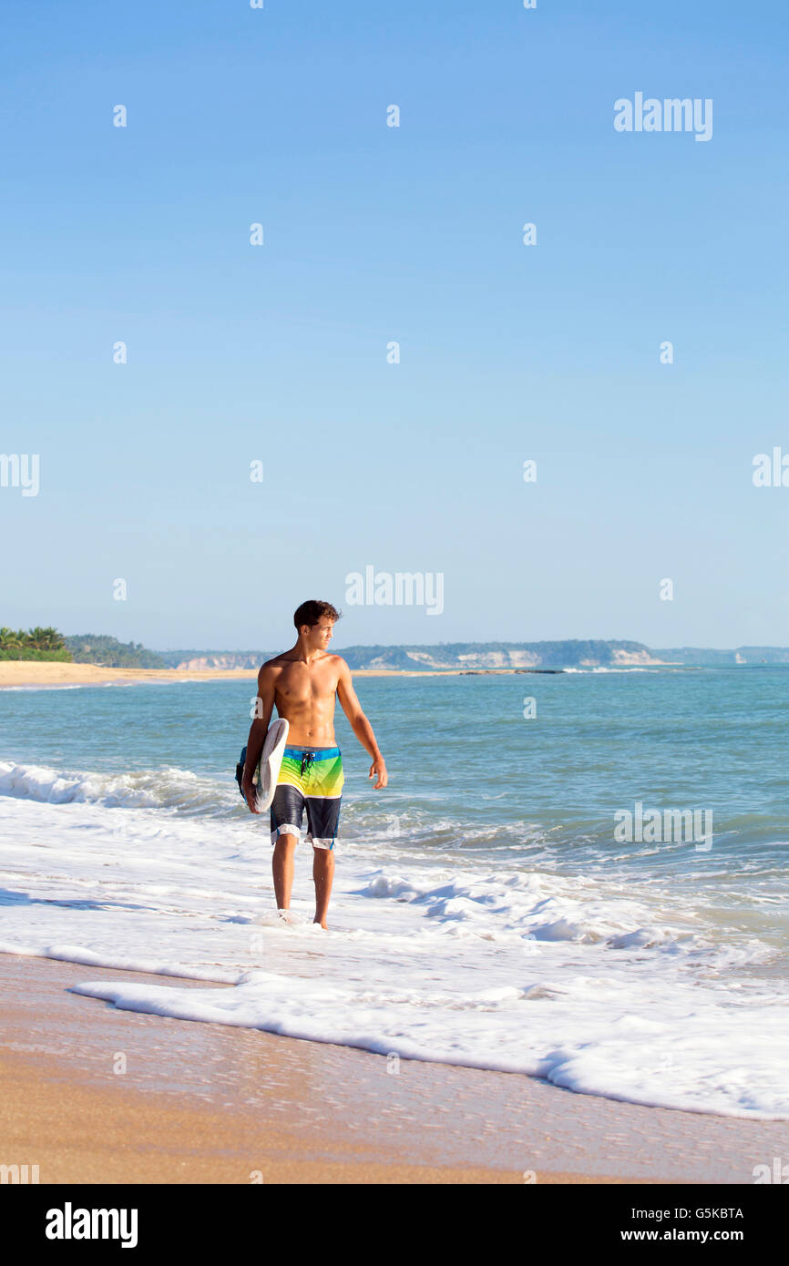Mixed race surfer carrying surfboard on beach Stock Photo