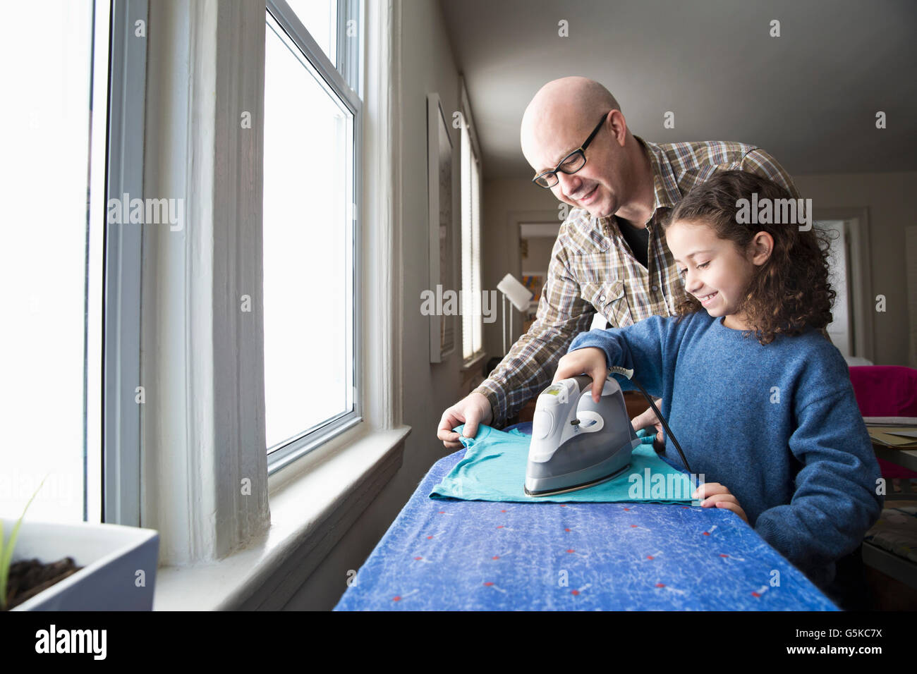 Father teaching daughter to iron fabric Stock Photo