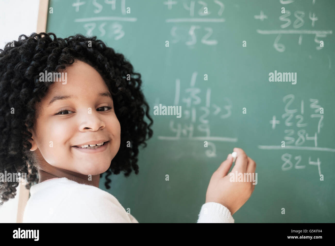 African American student writing on chalkboard in classroom Stock Photo