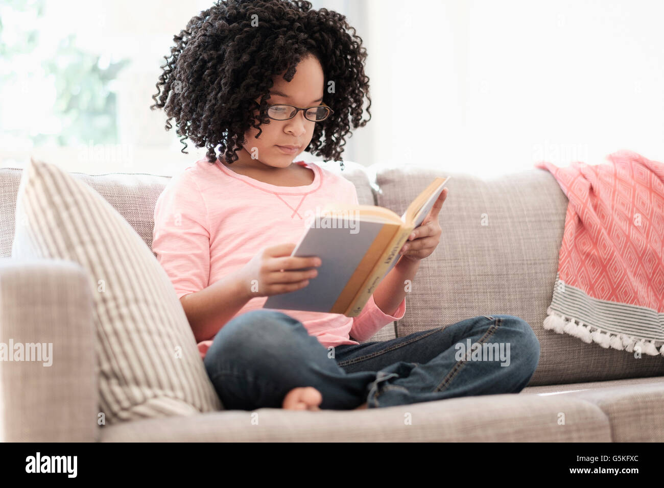 African American girl reading book on sofa Stock Photo
