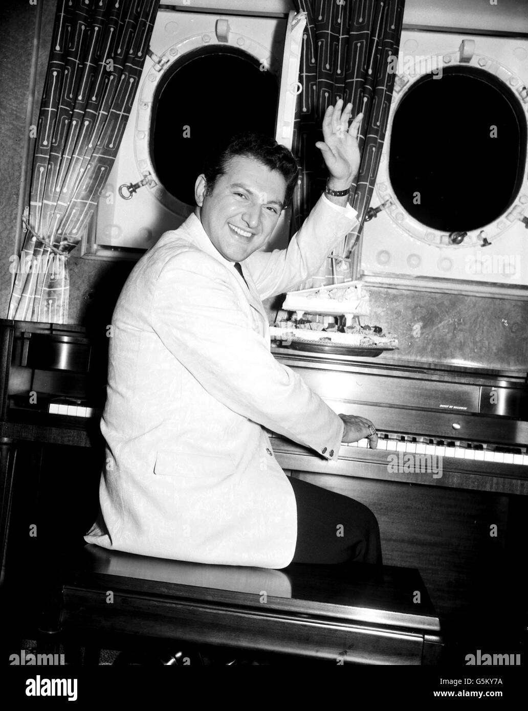 The well known smile and the twinkling fingers on the keyboard are seen in Britain again as American pianist Liberace arrives at Southampton aboard the Cunard liner Queen Elizabeth. Stock Photo