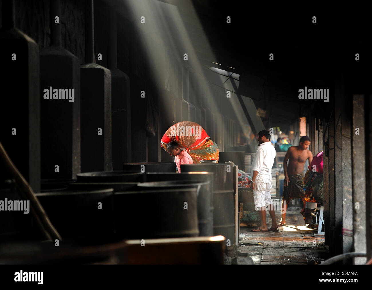 A man carries clothes past boiling drums as washers, known locally as Dhobis, work in the open to wash clothes from Mumbai's households, hotels and hospitals at the Mahalaxmi Dhobi Ghat (washing place) in the Mahalaxmi district of Mumbai, India. Stock Photo