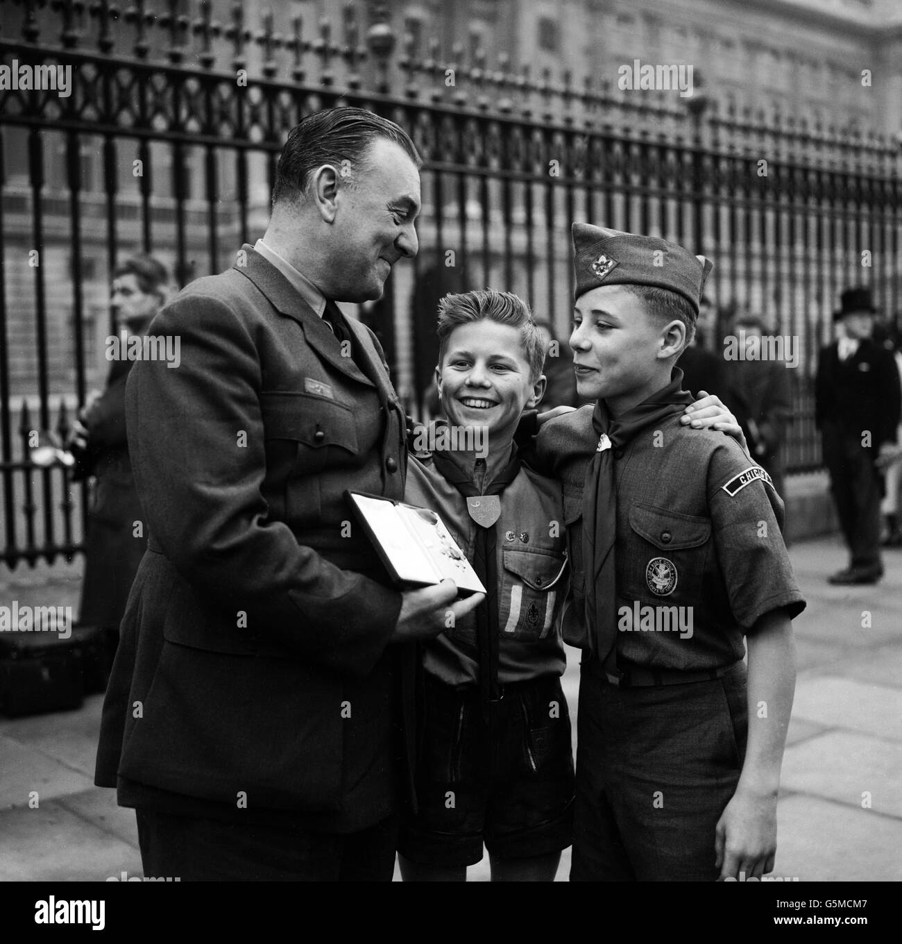 Ralph Reader, whose 'Gang Show' was presented at the Royal Variety Performance leaves Buckingham Palace after taking part in another Royal occasion. * ... He had just received the CBE (Commander of the British Empire Order) from the Queen at an investiture and he is seen showing the insignia to Scouts Mickie Hannam (left) and John Robinson. Stock Photo