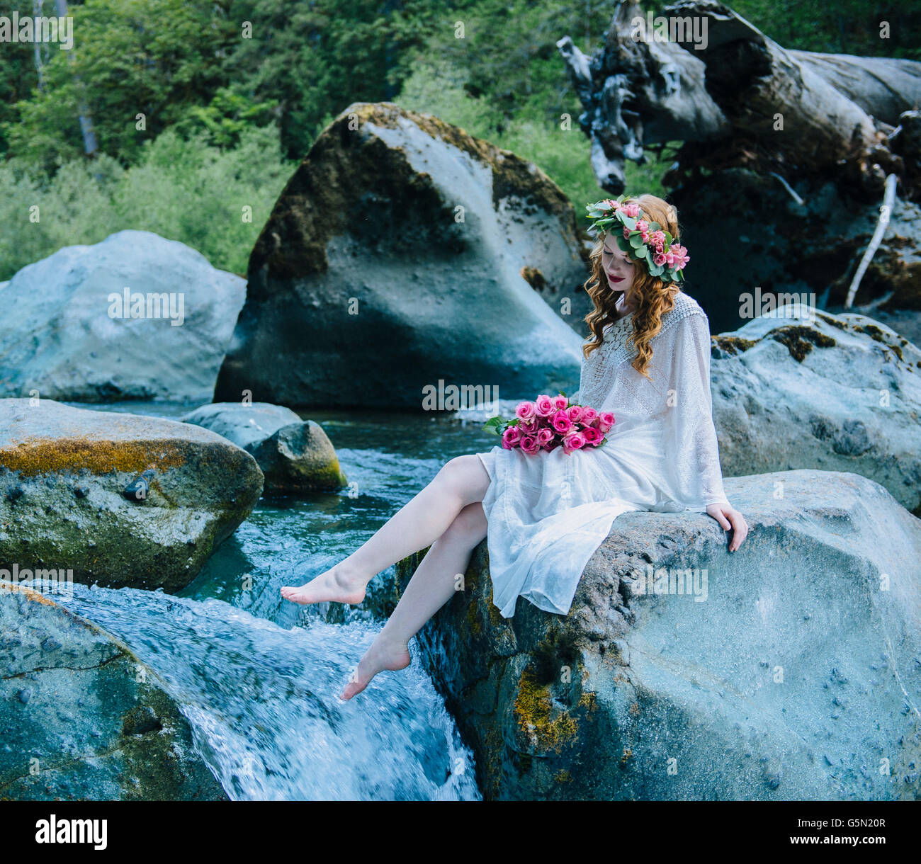 Caucasian woman wearing flower crown on rock at river waterfall Stock Photo