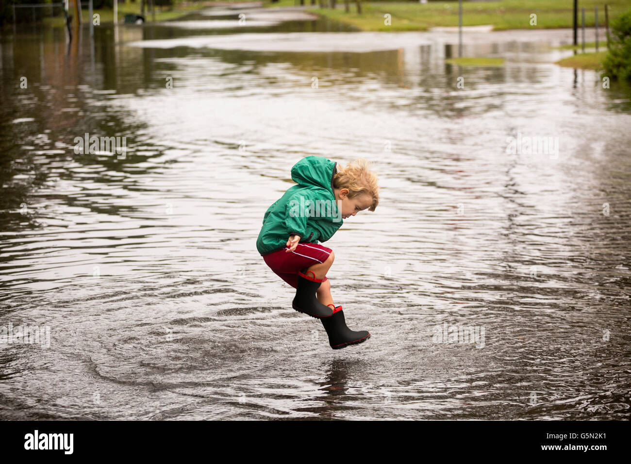 Caucasian boy jumping in puddle Stock Photo