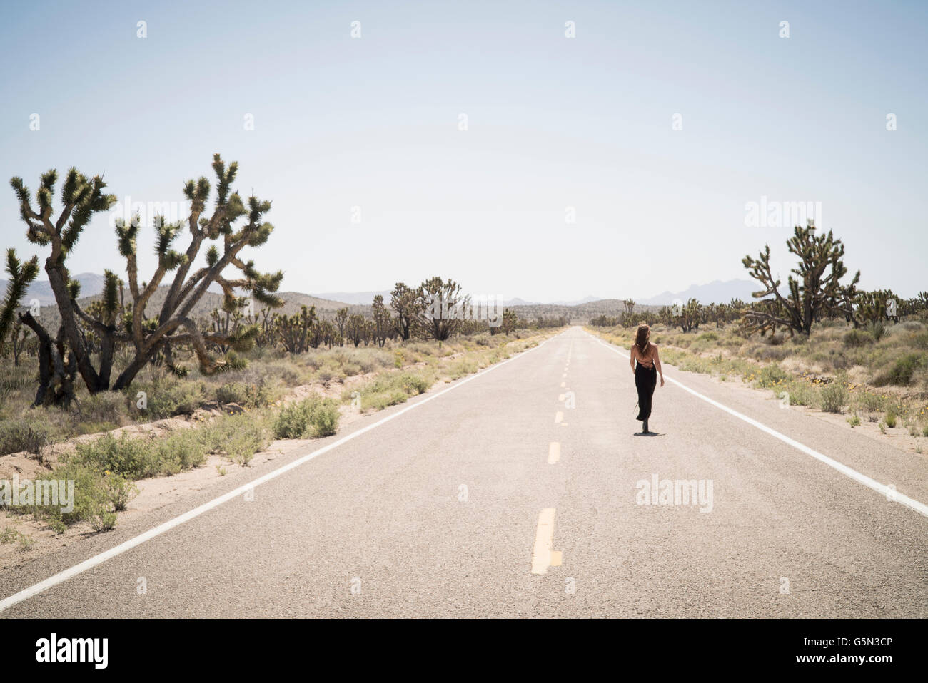Caucasian woman walking on remote desert road Stock Photo