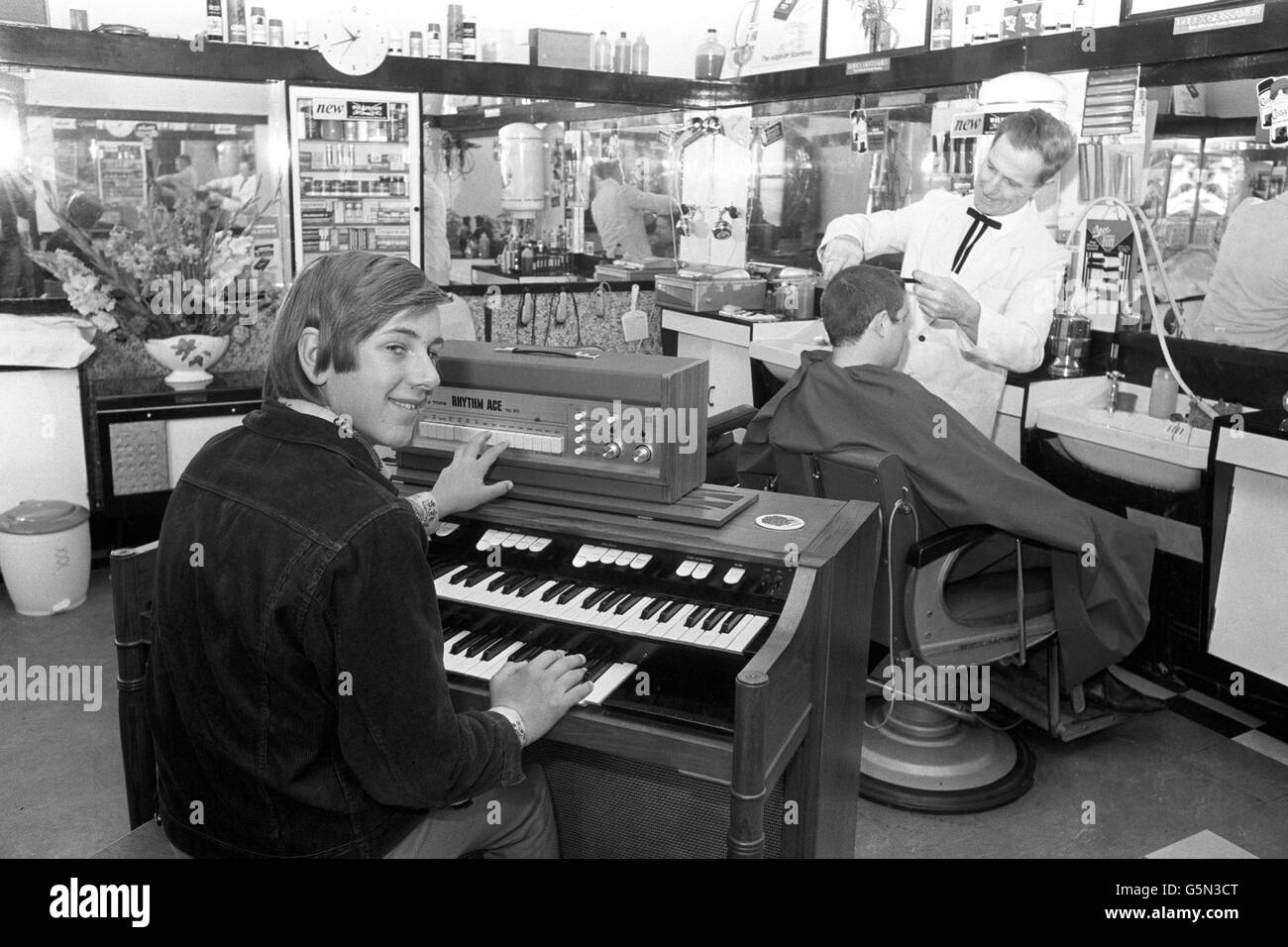 A customer plays an electric organ as he waits for his turn in the barber's chair at Clif Reynold's hairdressing salon in Withington, Manchester. Stock Photo