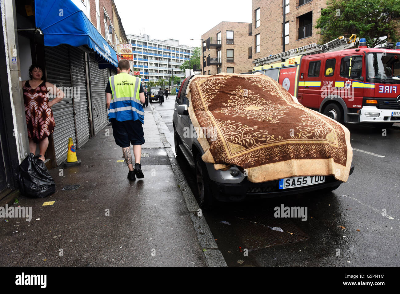 East London flooding: Residents drying wet carpet on top of the car after  the house flooding caused by heavy rains in East London, Canning Town. Fire  Brigade vehicle seen behind Stock Photo -