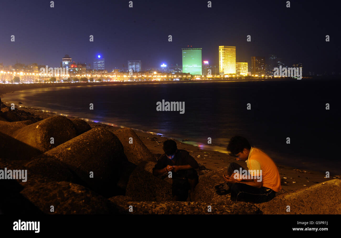 Two boys use mobile phones on the rocks of Marine Drive as Nariman Point is seen in the distance in Mumbai, India Stock Photo