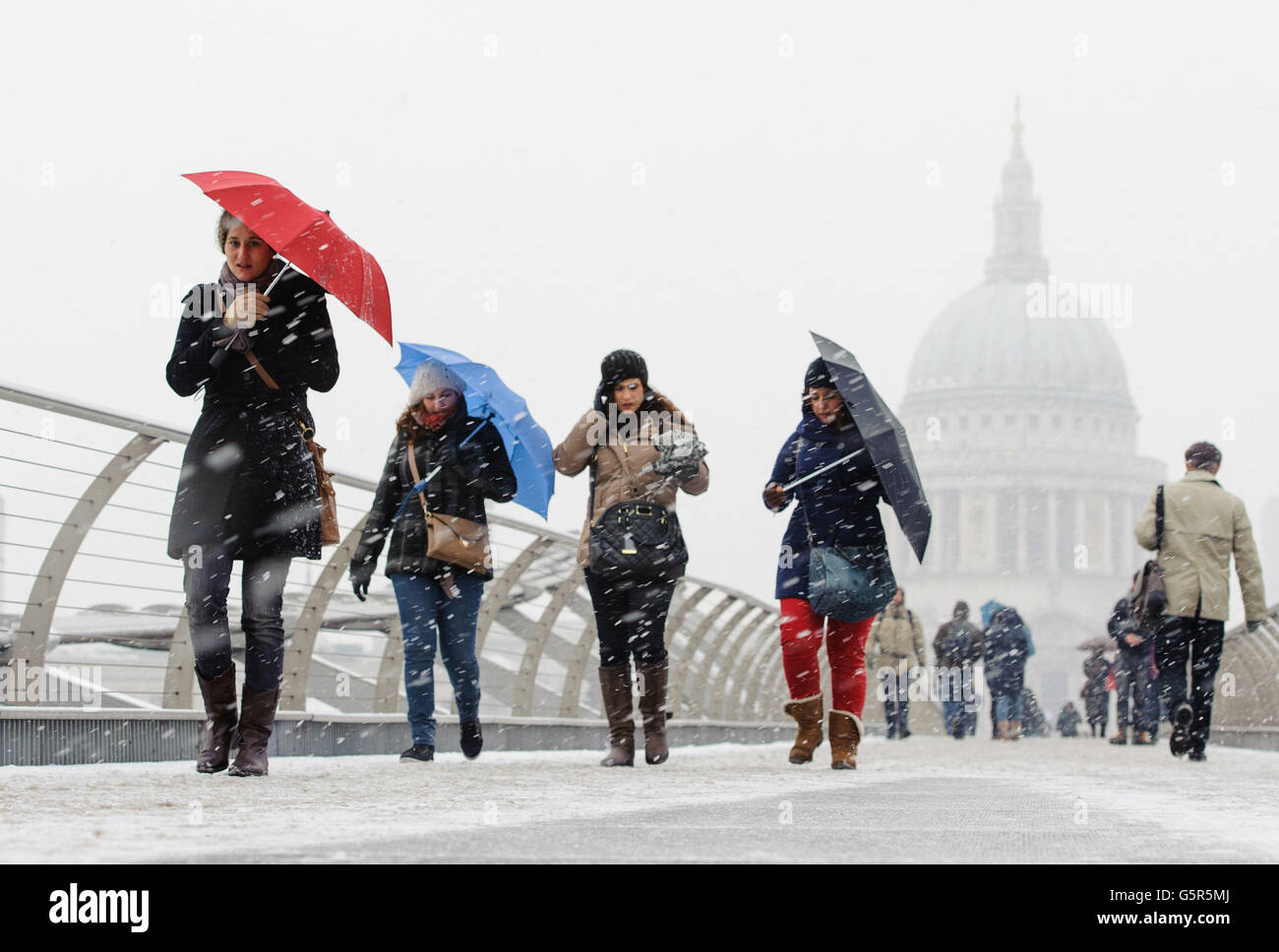 Pedestrians cross the Millennium Bridge, near St Paul's Cathedral, as snow falls in central London. Stock Photo
