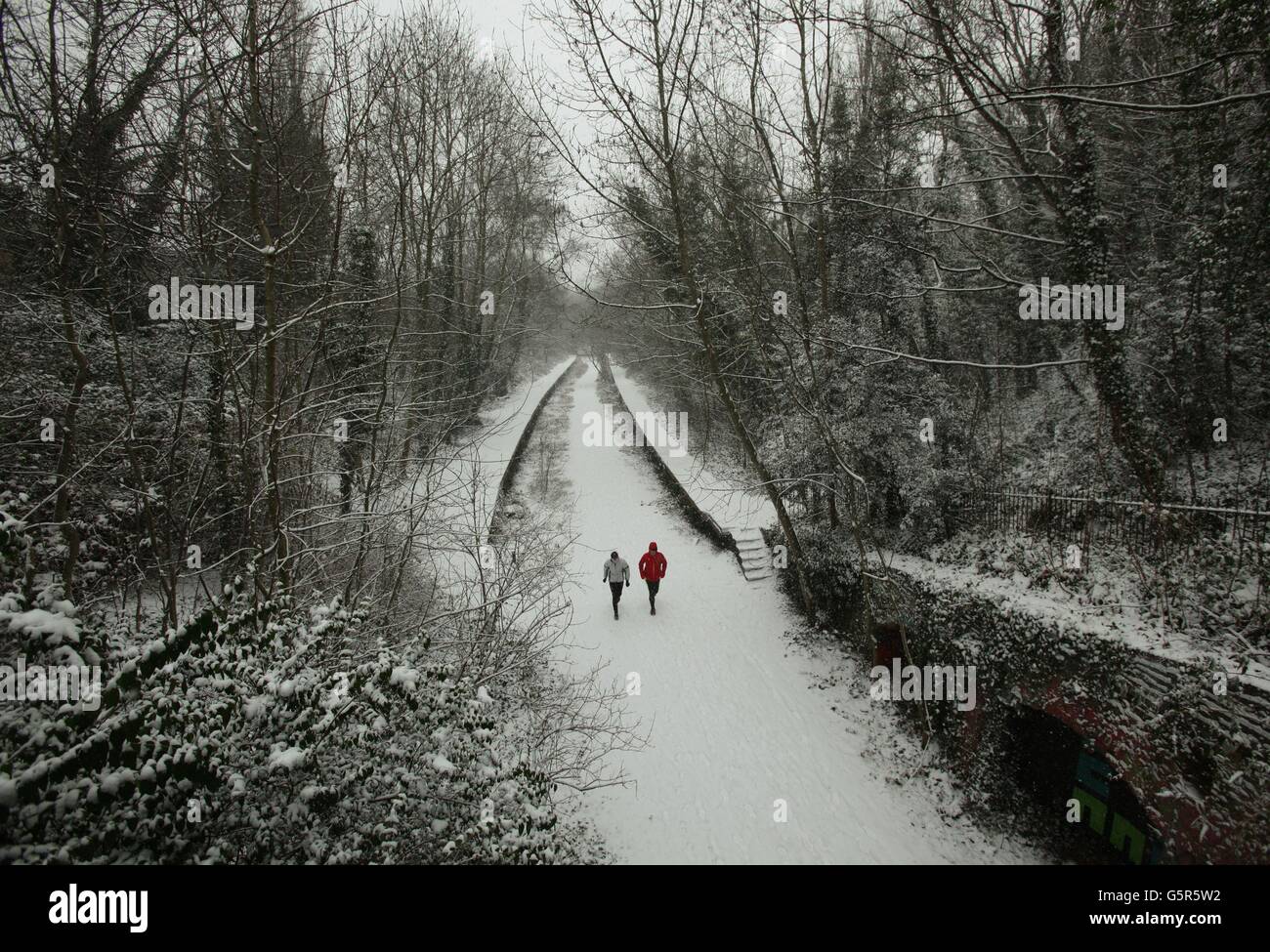 Joggers in the snow along the Parkland Walk nature reserve trail, in north London. Stock Photo
