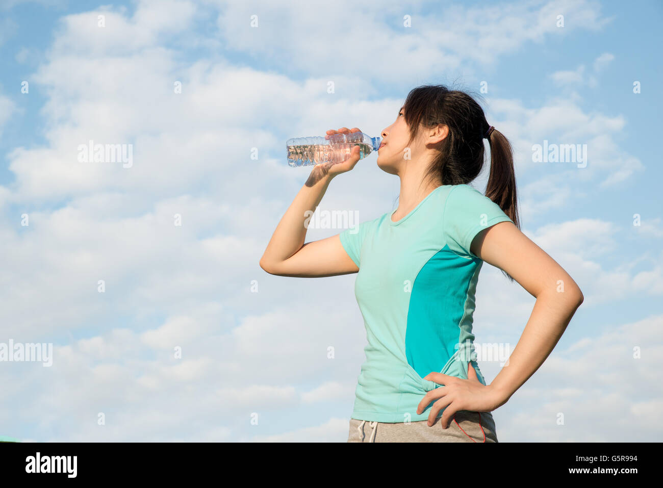 Sport Woman - Asian young woman drinking water during morning jogging. Asian woman drinking water from bottle. Stock Photo