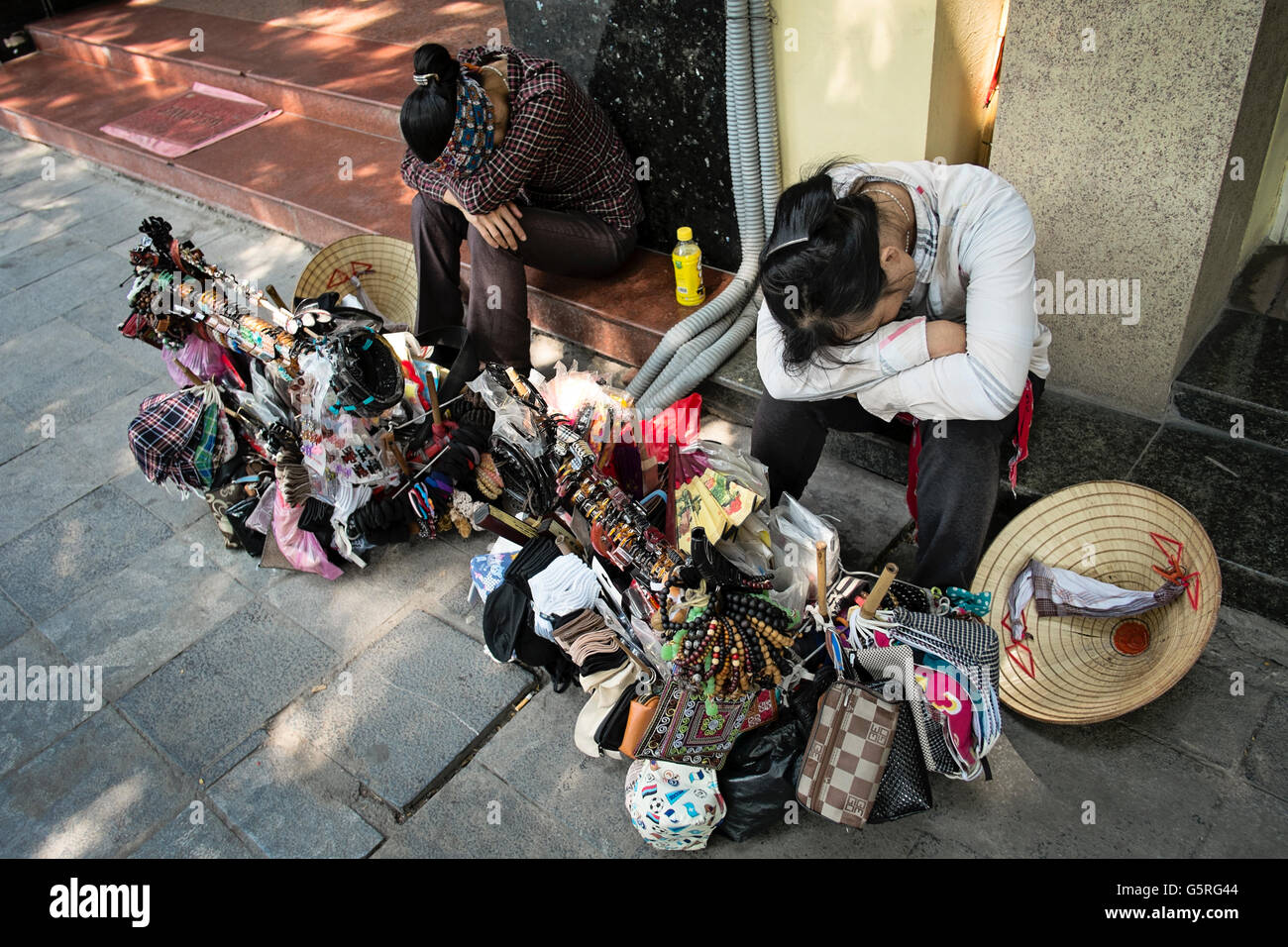 Two young women who sell tourist gifts, rest on the steps of a building in the Old District of Hanoi, Hoan Kiem, Vietnam. Stock Photo