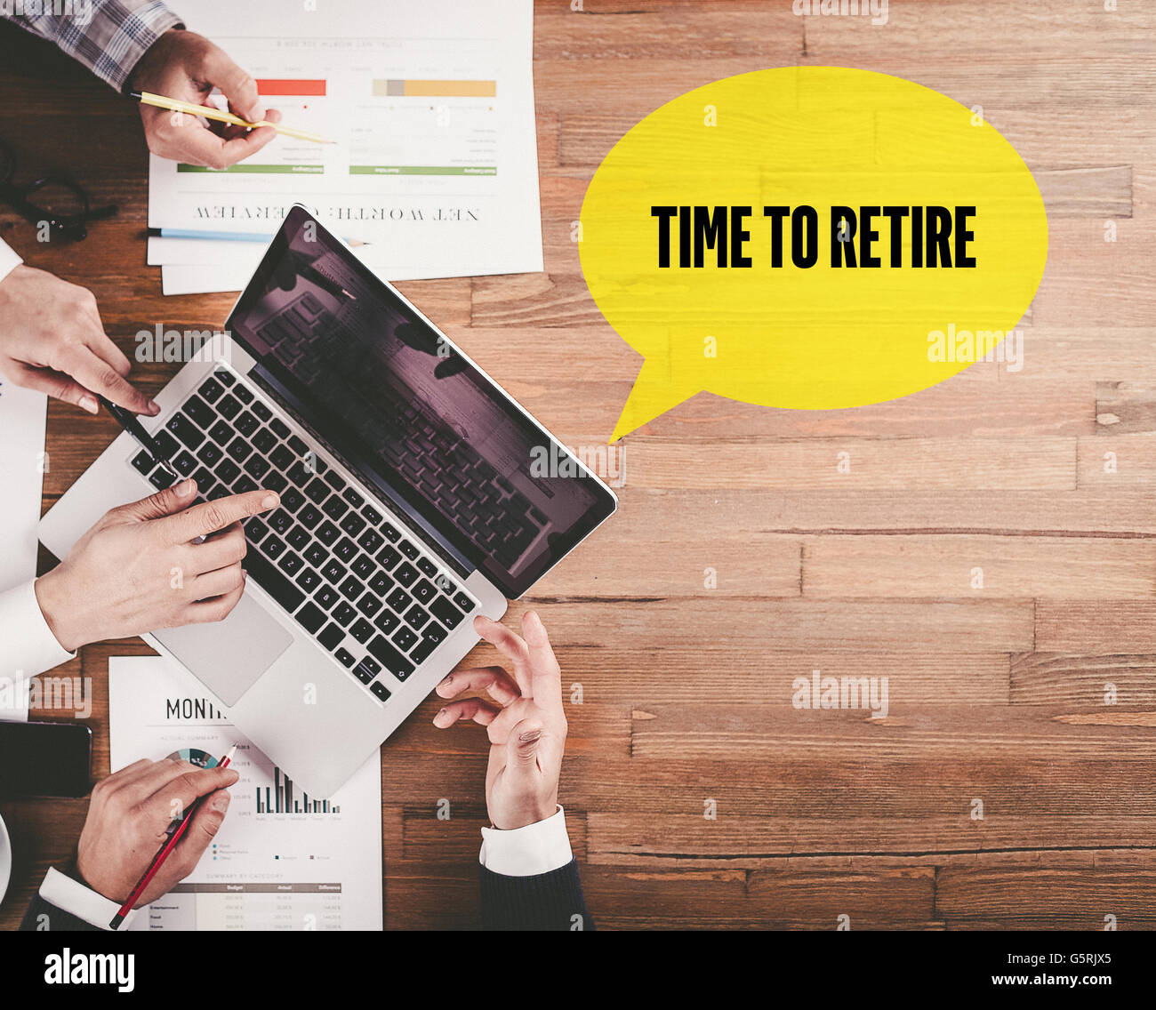 BUSINESS TEAM WORKING IN OFFICE WITH TIME TO RETIRE SPEECH BUBBLE ON DESK Stock Photo