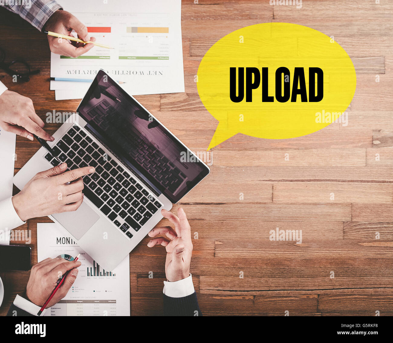BUSINESS TEAM WORKING IN OFFICE WITH UPLOAD SPEECH BUBBLE ON DESK Stock Photo