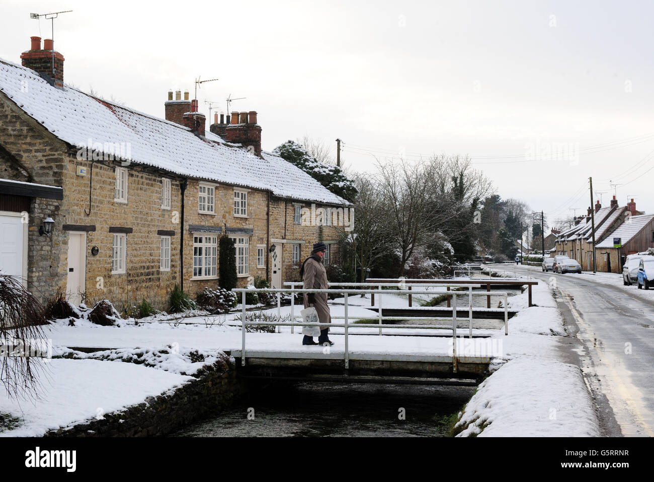 A woman walks past snow covered cottages at Thornton Le Dale, Pickering, North Yorkshire. Stock Photo