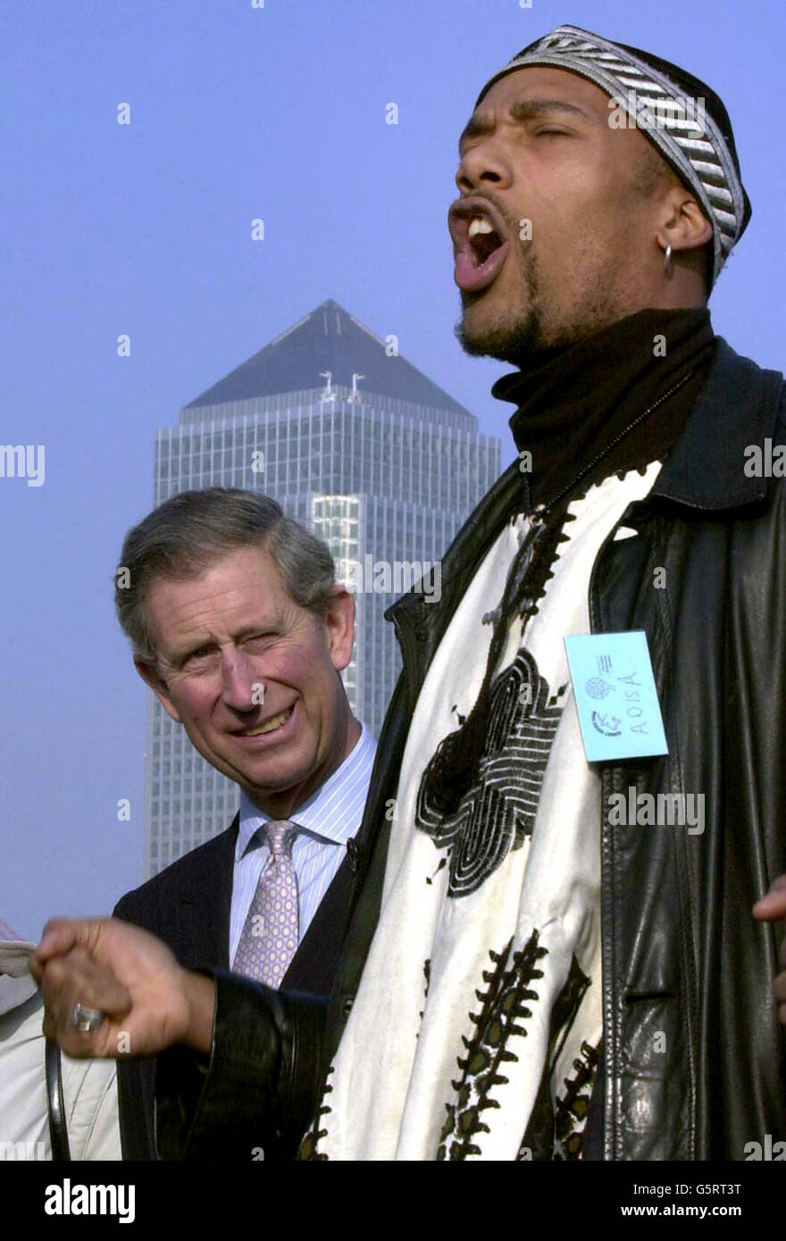 The Prince of Wales listens to poet, Adisa, sing a luck poem, with Canary Wharf behind him, during a visit to Surrey Docks City Farm, South East London. Stock Photo