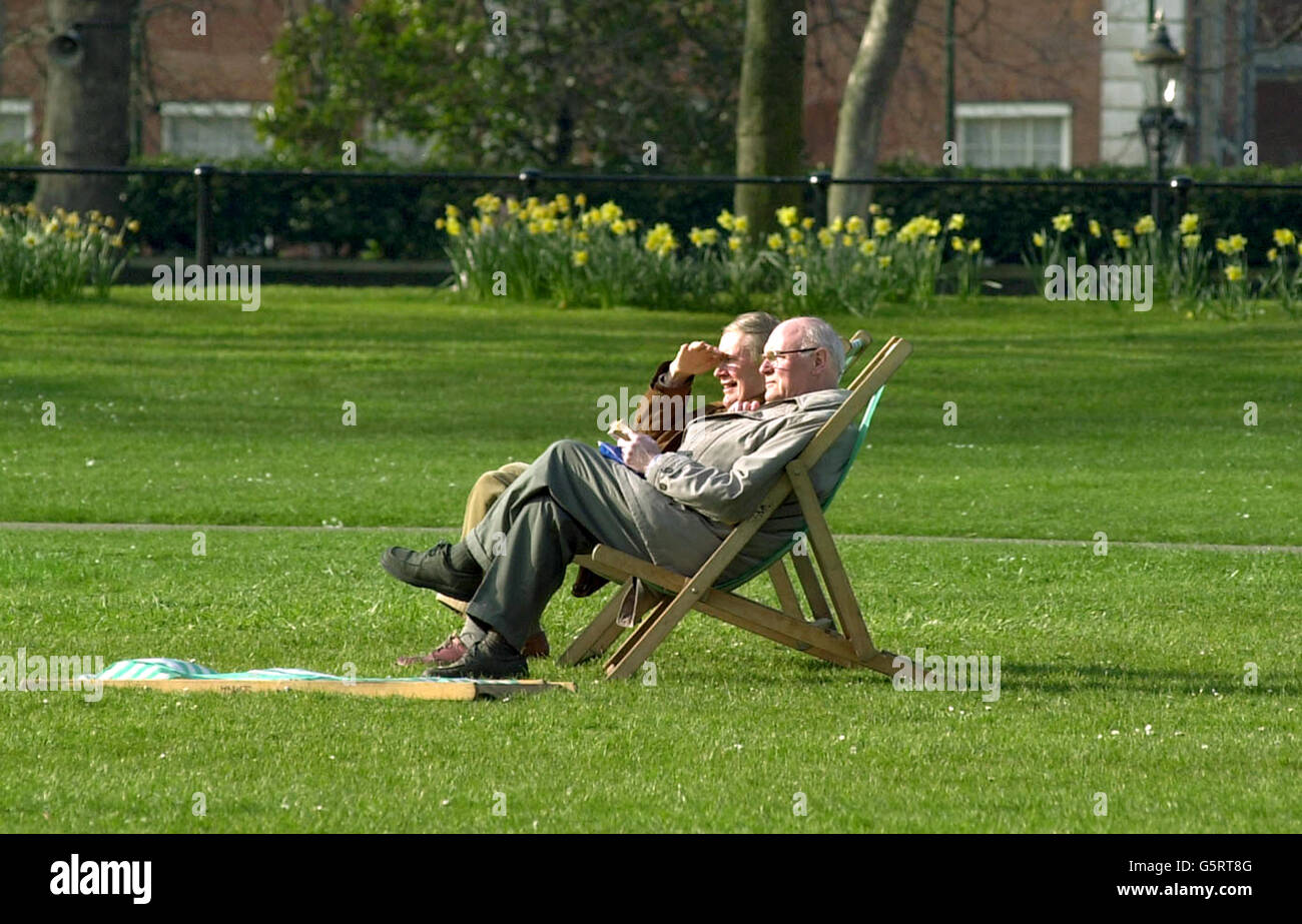 Two men sit in deckchairs in Green Park in central London, enjoying