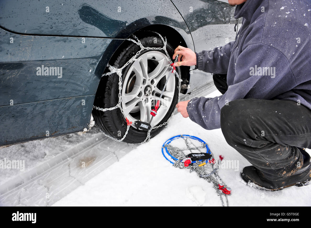 A man (POSED BY MODEL) fits THULE CG-9 Snow-Chains to a BMW rear wheel drive vehicle to help driving through snow, especially on rear wheel drive vehicles, which are much more prone to becoming stuck due to loss of traction. Stock Photo