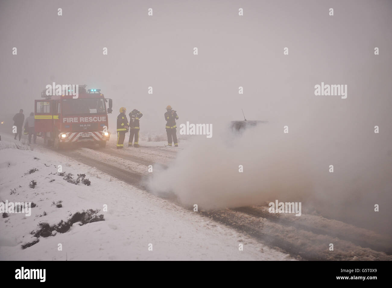 Firefighters extinguish a car fire on a hill on the B3212 at Dartmoor, Devon, after its driver Matthew Shipton 21, from Callington, was driving home from his workplace at Bovey Castle after they let him finish four hours early due to the bad weather conditions. Stock Photo